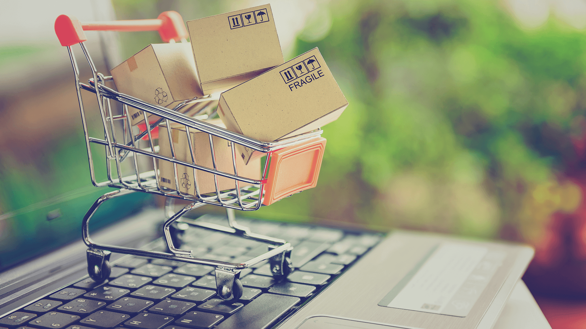 Mini carrinho de compras cheio de caixas em cima de um notebook.